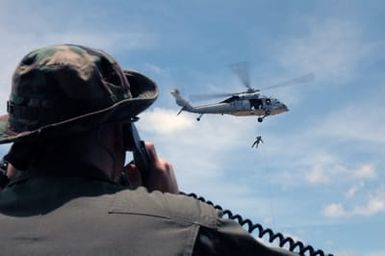 US Navy (USN) PETTY Officer Second Class (PO2) Justin Birch, utilizes a portable field radio to talk communicate with a USN MH-60S Sea Hawk helicopter from Helicopter Sea Combat Squadron 25 (HSC-25), as Royal Australian Navy (RAN) Sailors and USN Sailors conduct rappel training during a Helicopter Rope Suspension Technique (HRST) training exercise held at Polaris Point, Santa Rita Naval Base, Guam (GU), during the Annual Multi-national Explosive Ordnance Disposal (EOD) Exercise known as TRICARB 2006." The Exercise brings together EOD Units from the US, Australia and Singapore