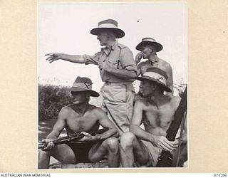 YULE ISLAND, NEW GUINEA. 1944-05-17/18. SERGEANT BROADHURST, AUSTRALIAN NEW GUINEA ADMINISTRATIVE UNIT (1), INDICATES MOVEMENT ON THE BANK TO MEMBERS OF THE 1ST MARINE FOOD SUPPLY PLANTOON, WHO ARE ..