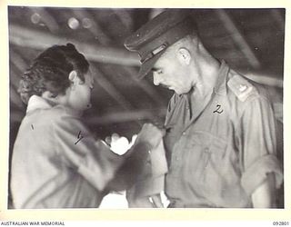 LAE, NEW GUINEA. 1945-06-09. PRIVATE EVANS (1), TYING RECORDS AND EMBARKATION DETAILS ON THE SHIRT OF MAJOR V.J.M. TRUDA (2), WHO IS EMBARKING WITH 2/7 GENERAL HOSPITAL PATIENTS ON THE HOSPITAL ..