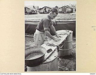 CAPE WOM, WEWAK AREA, NEW GUINEA. 1945-09-15. DRIVER E.F. PEARCE, HEADQUARTERS 6 DIVISION, SCRUBBING CLOTHES ON A WASHING BENCH