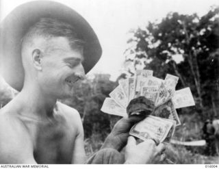 Guy's Post, Ramu Valley, New Guinea. October 1943. Private J. Morris of Semaphore, SA, with Japanese "invasion money" found after the Japanese were driven from this area