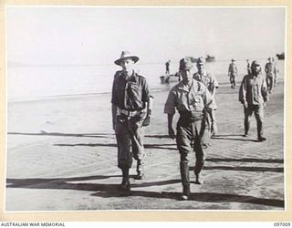 CAPTAIN W. DAVIES, MEMBER OF THE AUSTRALIAN SURRENDER PARTY FROM HEADQUARTERS 2 CORPS, ACCOMPANIED BY MAJOR GENERAL K. KIJIMA, WALKING ACROSS THE BEACH TOWARDS THE CONFERENCE HUT. THE SURRENDER ..