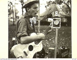 GUSIKA, NEW GUINEA, 1944-03-17. V125901 PRIVATE W. ROBINS, 29/46TH INFANTRY BATTALION, 4TH INFANTRY BRIGADE, PLAYS A SPANISH GUITAR MADE FROM A BISCUIT TIN. HE IS A MEMBER OF "TRENKNER'S TROUBADOUR ..