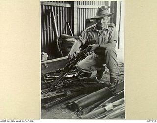 LAE BASE AREA, NEW GUINEA. 1944-12-27. WX32312 LIEUTENANT W.J. HARRIGAN, OFFICER- IN- CHARGE, 3RD CORPS SALVAGE UNIT, CHENCKING JAPANESE SMALL ARMS AND SUTOMATIC WEAPONS