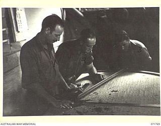 LAE, NEW GUINEA, 1944-03-29. THREE OF THE TEN MEN WHO MAN THE BATTERY PLOTTING ROOM AT N HEAVY BATTERY, ROYAL AUSTRALIAN ARTILLERY ATTACHED TO HEADQUARTERS LAE BASE SUB-AREA. THIS ROOM, WHERE ALL ..