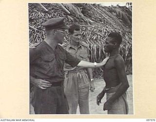 MAPRIK, NEW GUINEA. 1945-10-03. A NATIVE EXPLAINING TO CAPTAIN M. VERSO, MEDICAL OFFICER, AUSTRALIAN NEW GUINEA ADMINISTRATIVE UNIT HEADQUARTERS, THAT HE IS "ALL IN, AND VERY SICK"