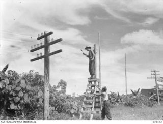 TOROKINA, BOUGAINVILLE ISLAND. 1945-01-18. NX191264 SIGNALLER F.M. NUTTALL (1) ASSISTING QX45030 CORPORAL D.W. BILL (2) WHO IS SOLDERING AN EARTH WIRE TO A NEUTRAL POINT ON THE SET OF WIRES WHICH ..