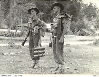 WUNUNG PLANTATION, JACQUINOT BAY, NEW BRITAIN. 1945-02-01. WX29776 SERGEANT R. MCCAUGHAN, 16TH INFANTRY BATTALION (2) DEMONSTRATING A NEW METHOD OF CARRYING 3" MORTAR BOMBS WHICH HE HAS DEVISED. ON ..