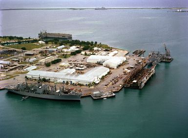 A starboard view of the combat stores ship USS NIAGARA FALLS (AFS 3) moored at the US Naval Ship Repair Facility. A floating dry dock and two frigates are in the background