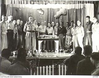 LAE BASE AREA, NEW GUINEA. 1944-12-27. VX104118 MAJOR R. UPSON ANNOUNCING THE RESULT OF A COLLECTION FOR THE MOTHER OF A DECEASED MEMBER OF THE UNIT AT A CHRISTMAS CONCERT HELD IN THE AUDITORIUM OF ..