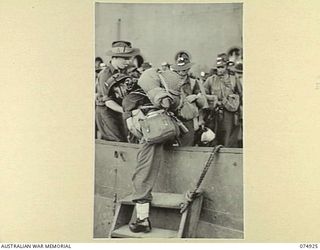 SIAR, NEW GUINEA. 1944-07-25. TROOPS OF THE 61ST INFANTRY BATTALION, HAMPERED WITH THEIR GEAR, BEING ASSISTED FROM THE PONTOON INTO THE LANDING BARGES AFTER DISEMBARKING FROM THE TRANSPORT SHIP ..