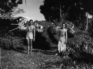 [Portrait of two Pacific Island men holding baskets on their shoulders]