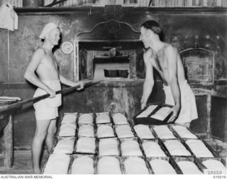 1943-06-15. NEW GUINEA. A.I.F. BAKERS AT WORK IN NEW GUINEA. PTE. G.I. HALL, OF BALEKLAVA, SOUTH AUSTRALIA HANDS OVER THE DOUGH TO CPL. M.R. COWLEY OF ARNO BAY, SOUTH AUSTRALIA. (NEGATIVE BY N. ..