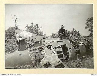 HOSKINS, NEW BRITAIN. 1944-10-09. AN AUSTRALIAN SOLDIER EXAMINING A WRECKED JAPANESE AIRCRAFT ON THE EDGE OF THE AIRSTRIP