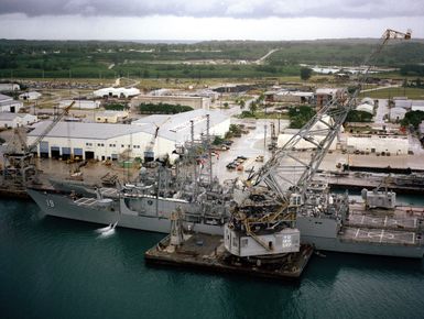 A partial port view of the guided missile frigate USS JOHN A. MOORE (FFG 19) docked at the US Naval Ship Repair Facility. A large crane (YD-120-SRF) is positioned alongside the frigate