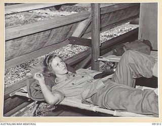 LAE, NEW GUINEA. 1945-05-07. PRIVATE G. HOOPER, RESTING ON A STRETCHER AFTER SETTLING IN AT THE NEWLY CONSTRUCTED AUSTRALIAN WOMEN'S ARMY SERVICE BARRACKS IN BUTIBUM ROAD. SHE IS ONE OF A GROUP OF ..