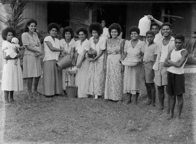 [Group of young pacific island girls and boys with vessels of water in front of a house]