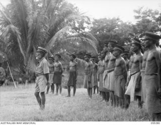 HOPOI, NEW GUINEA, 1943-10-30. CHIEFS OF THE VILLAGES IN THE AREA LISTENING TO AN ADDRESS BY NX155085 CAPTAIN R.G. ORMSBY OF THE AUSTRALIAN AND NEW GUINEA ADMINISTRATIVE UNIT. STANDING IN FRONT OF ..