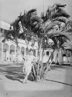 [Portrait of a woman by palms outside a building]