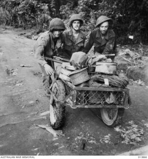 1942-12-17. PAPUA. AUSTRALIANS AND AMERICANS FOUGHT TOGETHER AT SANANANDA. HERE THEY ARE PUSHING A TRAILER FULL OF EQUIPMENT NEAR SANANANDA