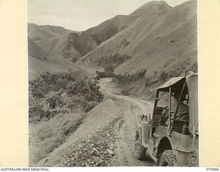 WAU - LAE ROAD, NEW GUINEA, 1944-02-26. THE ROAD SECTION 32 MILES FROM WAU RUNNING NORTH DOWN THE WATUT VALLEY 200 FEET ABOVE THE LEVEL OF THE RIVER. THE MOUNTAIN FROM WHICH THE ROAD IS CUT, IS ..