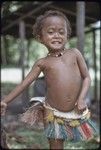 Young girl, Imala (daughter of Mogiovyeka), wearing short fiber skirt and shell necklace, dabs of betel-nut paste on her cheeks and nose