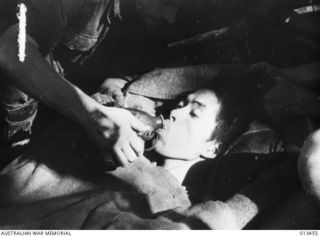 1942-10-19. NEW GUINEA. AUSTRALIAN TROOPS ADVANCE THROUGH OWEN STANLEY RANGES. JAP. PRISONER. THIS SOLDIER, LEFT TO DIE BY HIS COMRADES, IS GIVEN A DRINK BY AN AUSTRALIAN SOLDIER