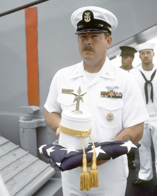 MCPO Charles Cartwright holds the urn containing the remains of CDR Harold Schwartz during burial at sea services aboard the tank landing ship USS RACINE (LST-1191), anchored off Guadalcanal in the Solomon Islands. Schwartz served as a doctor assigned to the Paratroop Battalion, 1ST Marine Division and took part in combat operations on Guadalcanal, the Gilbert Islands, Marshall Islands and Okinawa during World War II
