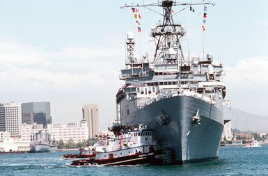 A commercial harbor tug maneuvers the miscellaneous flagship USS CORONADO (AGF-11)into port at Naval Air Station, North Island, San Diego. The CORONADO, flagship for Commander, Third Fleet, will be arriving at its new home port after being stationed in Hawaii for almost 20 years