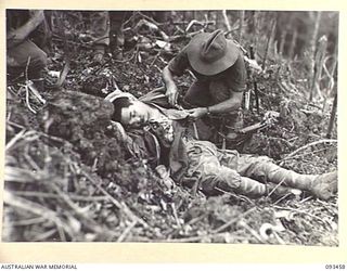 WEWAK AREA, NEW GUINEA, 1945-06-27. PTE V.R. MAURER, INTELLIGENCE SECTION, 2/8 INFANTRY BATTALION, SEARCHING A DEAD JAPANESE SOLDIER FOR DOCUMENTS. THE UNIT IS ADVANCING UP THE SIDE OF MOUNT ..