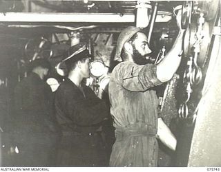 AT SEA. 1944-08/09. ENGINE ROOM ARTIFICERS WORKING IN THE ENGINE ROOM OF THE RAN CORVETTE, GEELONG AS THE VESSEL PROCEEDS ALONG THE COAST OF NEW GUINEA