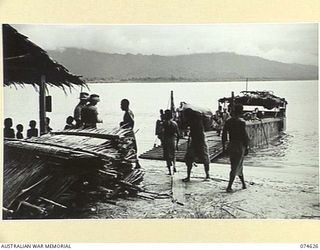 BASAMA-LAE AREA. NEW GUINEA. 1944-07-13. MEMBERS OF THE AUSTRALIAN NEW GUINEA ADMINISTRATIVE UNIT CHECKING ROOF THATCHING MATERIAL (SAC-SAC) BEING UNLOADED FROM A BARGE BY BASAMA NATIVES