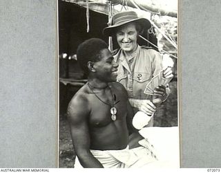 HELDSBACH PLANTATION, NEW GUINEA. 1944-04-06. 417 LANCE-CORPORAL WILLIAM MATPI, DCM, (1), ASSISTED BY SENIOR SISTER E.B.Y. CAMERON (2), AUSTRALIAN ARMY NURSING SERVICE DURING A GAME OF CARDS