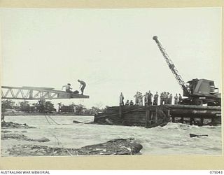 LAE, NEW GUINEA. 1944-08-09. TROOPS OF THE 20TH FIELD COMPANY, MAKING FAST THE END OF A STEEL BOX GIRDER TO THE CRANE WHICH IS TO HAUL THE GIRDER ACROSS THE GAP WHERE THE OLD WOODEN BRIDGE WAS ..