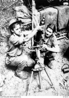 1943-08-30. NEW GUINEA. PTE. CHARLES WALKER OF ARMADALE, VICTORIA, AND PTE. CECIL ROBINSON OF ST. ARNAUD, VIC., LOADING A THREE INCH MORTAR ON MOUNT TAMBU. IN THE BITTER FIGHTING IN THIS AREA BOTH ..