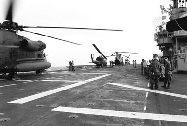 Flight operations take place aboard the amphibious assault ship USS GUAM (LPH 9) off the coast of Grenada during Operation URGENT FURY. Visible on the flight deck are two UH-1N Iroquois helicopters, a CH-46 Sea Knight helicopter and a CH-53 Sea Stallion helicopter