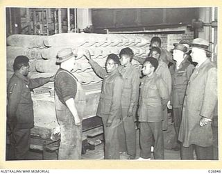 MARIBYRNONG, AUSTRALIA. 1942-10-12. A PARTY OF SIX PAPUAN NATIVE SOLDIERS BEING SHOWN OVER THE MUNITION WORKS SEE A STACK OF HEAVY CALIBRE SHELLS READY FOR DESPATCH TO THE FIGHTING AREAS