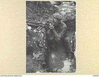 BOUGAINVILLE ISLAND, 1945-01-21. Q36799 CORPORAL J.J. BEATON, 42ND INFANTRY BATTALION LIGHTS A CIGARETTE IN HIS WATER FILLED FOXHOLE AFTER AN ALL NIGHT VIGIL AGAINST POSSIBLE JAPANESE INFILTRATION