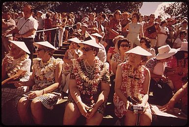 TOURISTS AT A HULA DANCE DEMONSTRATION. THOSE WHO DO THE DANCE ARE REWARDED WITH LEIS