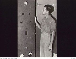 LAE, NEW GUINEA. 1945. SERGEANT K. SMITH, ANNOUNCER, FORMERLY OF RADIO STATION 3DB, MELBOURNE, VIC, INSPECTING THE CONTROL PANEL OF RADIO LAE, A 50-KILOWATT RADIO TRANSMITTER WHICH HAS BEEN MADE ..