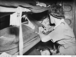 AIRBORNE, LAE, NEW GUINEA TO TOWNSVILLE, 1945-11-26. SISTER J. MENZIES, RAAF NURSING SERVICE (RAAFNS), ATTENDING TO SERGEANT L. TEAGUE, AWAS, A PATIENT OF 2/7 GENERAL HOSPITAL WHO IS BEING ..