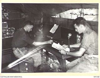 CAPE WOM, NEW GUINEA. 1945-09-29. AT RADIO 6 DIVISION, HEADQUARTERS 6 DIVISION, SIGNALMAN E.J. BULLEN IS AT THE TURNTABLE CONTROLS, PLAYING RECORDS, AND CORPORAL C.C. CHAPLIN IS MAKING AN ..