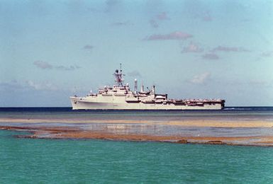 A port beam view of the Third Fleet flagship USS CORONADO (AGF-11) departing Pearl Harbor through the channel.