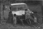 Truck with rust and other damage, pushed by woman and children