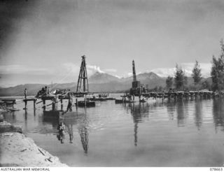 MOTUPENA POINT, BOUGAINVILLE ISLAND, 1945-01-26. SAPPERS OF THE 23RD COMPANY, WORKING ON THE CONSTRUCTION OF A PERMANENT TIMBER PILE BRIDGE ACROSS THE JABA RIVER. THE PONTOON FERRY WHICH IS TO BE ..