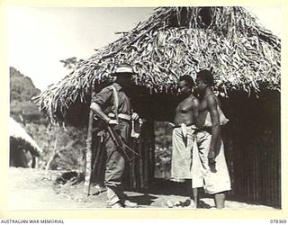 SAMPUN, NEW BRITAIN. 1945-01-15. CORPORAL L.S. MORGAN, 5TH MILITARY HISTORY FIELD TEAM ATTACHED TO HEADQUARTERS, 5TH DIVISION, CHATTING WITH HIS ALLIED INTELLIGENCE BUREAU NATIVE CARRIERS BEFORE ..