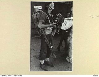 CAIRNS, QLD. 1944-10-28. PRIVATE "SQUEEZEBOX" N.J. BELLINGHAM, 2/4 INFANTRY BATTALION, AWAITS TO BOARD THE USS MEXICO DURING EMBARKATION FOR NEW GUINEA