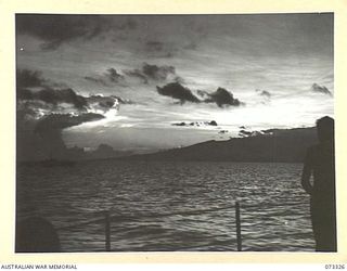 KARKAR ISLAND, NEW GUINEA. 1944-05-18. A CREW MEMBER ABOARD ONE OF HMA MOTOR LAUNCHES WATCHES DAWN BREAKING WEST OF THE ISLAND. JAPANESE POSITIONS ON THE ISLAND HAVE BEEN UNDER HEAVY BOMBARDMENT ..