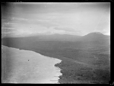 An aerial view of a coast airfield amongst palm trees near a village with beach slipways or piers, with forested mountains beyond, American Samoa