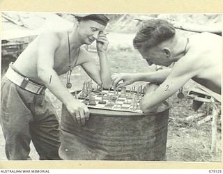 BOGIA, NEW GUINEA. 1944-07-30. NX121782 SERGEANT J.A. SIMS (1) AND N378137 PRIVATE R.W. WHIPP (2) OF THE 30TH INFANTRY BATTALION, ENGAGED IN A SERIOUS GAME OF CHESS AND USING A 44 GALLON DRUM AS A ..
